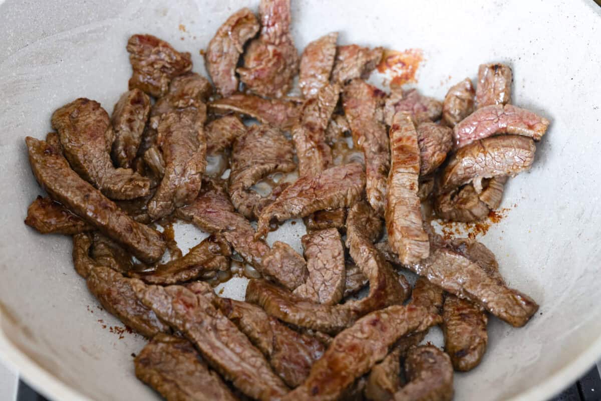Trust me on this one. If you want the most tender pepper steak you’ve ever made at home, this recipe is it. It’s fast, saucy, and I give you just enough tips to make it work on a busy night! Strips of steak cooking in a wok.
