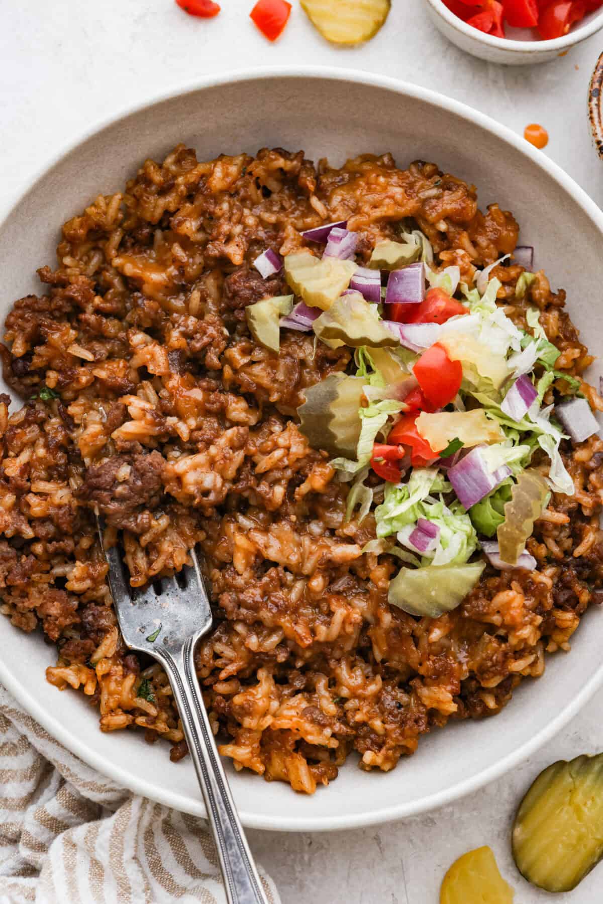 Cheeseburger rice is everything you love about a juicy cheeseburger, made easy in one skillet. Hearty, cheesy, and packed with flavor, itโs the ultimate weeknight comfort meal. Bowl of cheeseburger rice topped with lettuce, onion, tomato, lettuce and pickle.