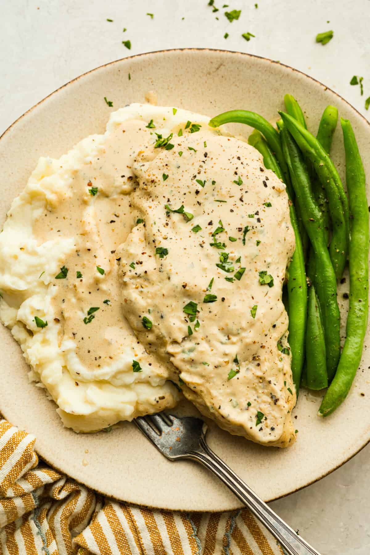 I'm excited for you guys to try this cream cheese chicken. It's an easy one-pan dinner with a rich, creamy sauce that delivers pure comfort food vibes. Itโs quick to make, easy to clean up, and perfect for cozying up on a busy night. Plated cream cheese chicken with mashed potatoes and green beans.