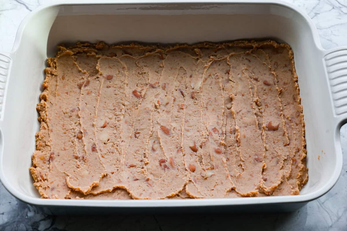 When you want enchiladas without the work, these Lazy Enchiladas are it! Four ingredients. Less than 30 minutes. Just layer frozen taquitos with beans, sauce, and cheese, bake until bubbly, and boom, dinner is served! Refried beans spread on the bottom of the baking dish.