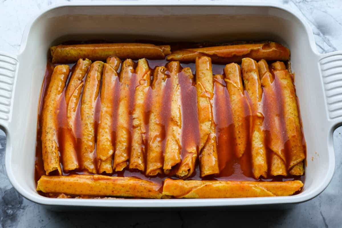 When you want enchiladas without the work, these Lazy Enchiladas are it! Four ingredients. Less than 30 minutes. Just layer frozen taquitos with beans, sauce, and cheese, bake until bubbly, and boom, dinner is served! Enchilada sauce spread over the top of the taquitos.
