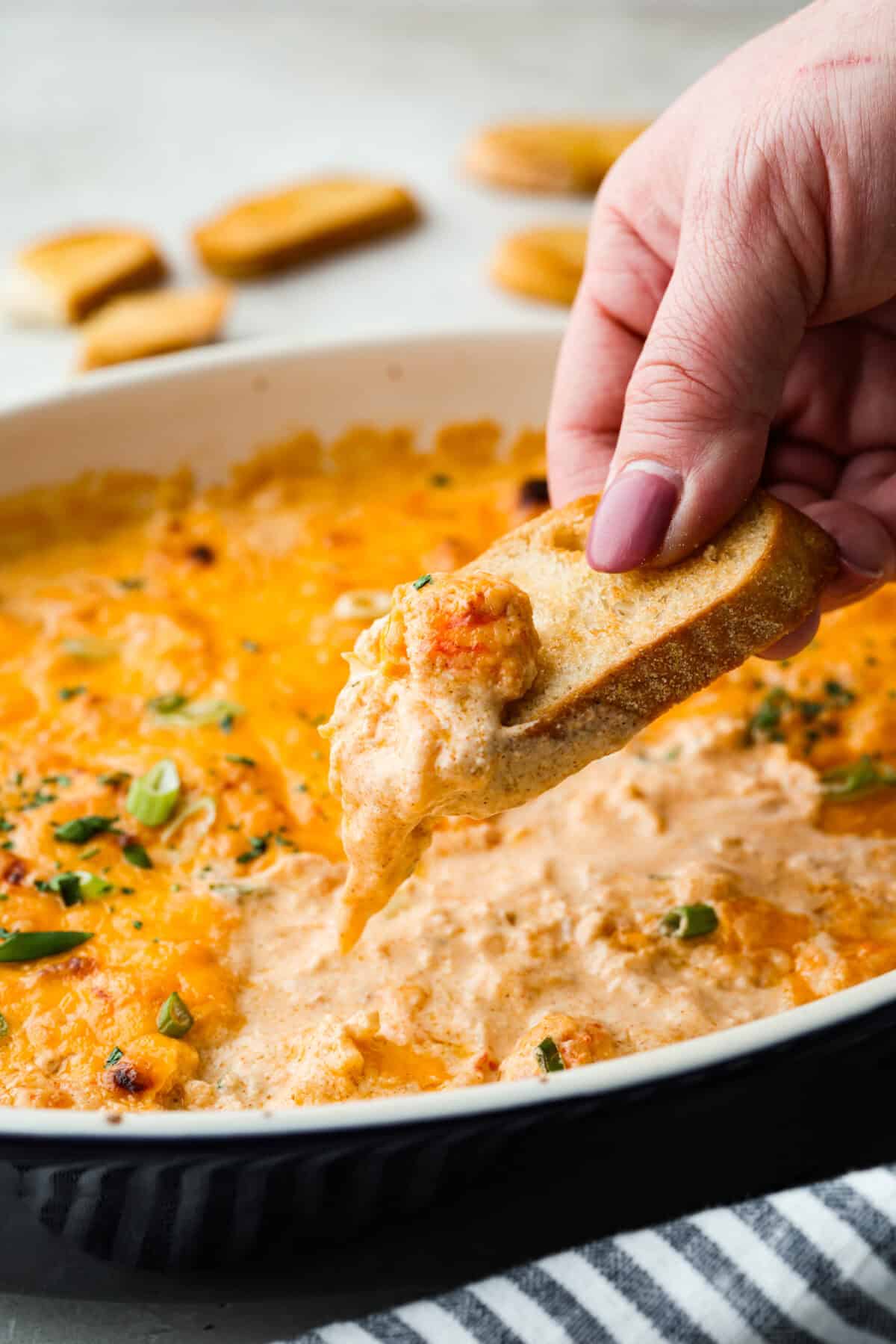 If you love a good lobster rolls, you’ll love it even more as a dip. Creamy, cheesy, and loaded with tender lobster, serve it warm, grab some crackers or bread, and let the dipping begin! Someone scooping lobster roll dip with a crostini.
