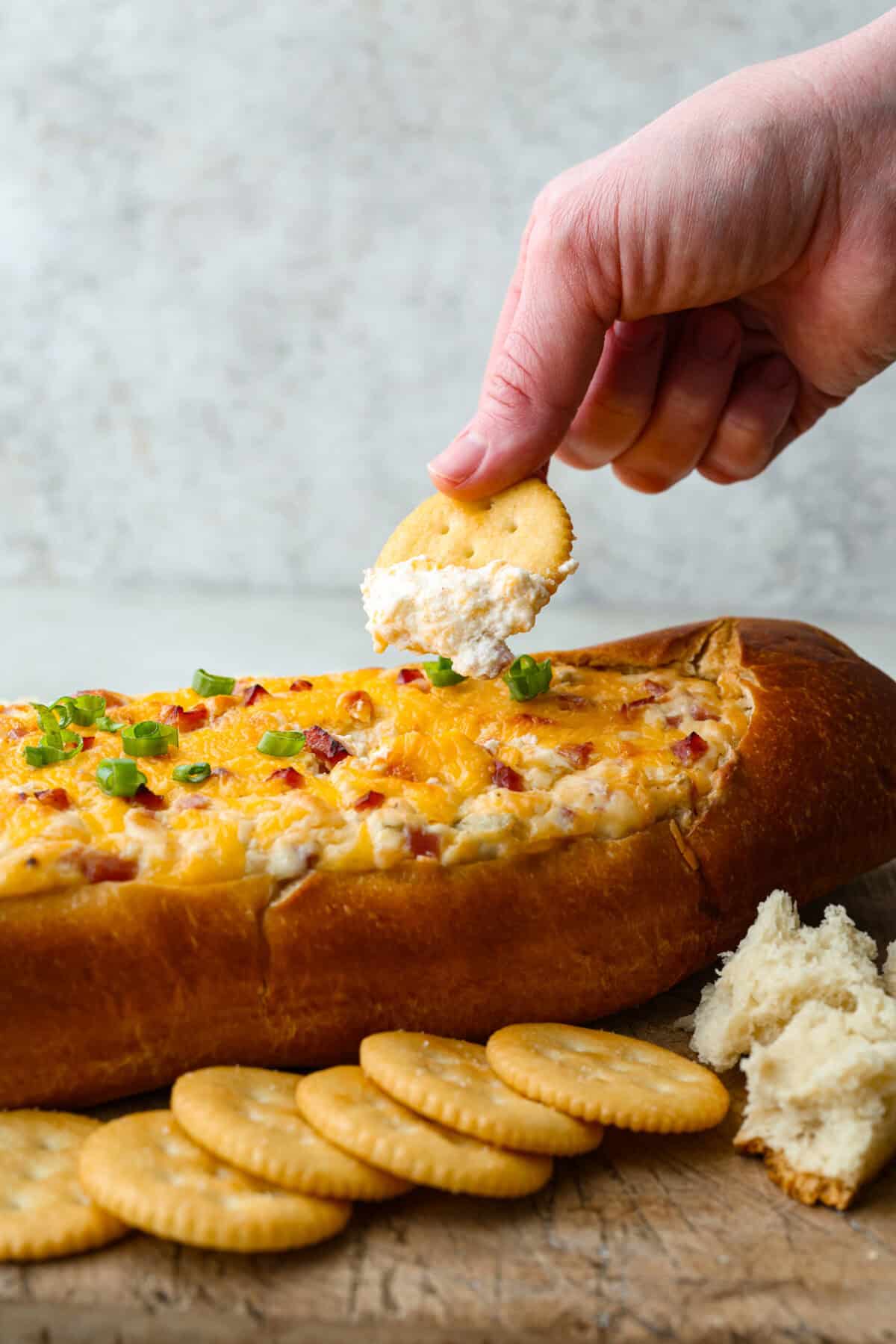 This Mississippi sin dip is pure comfort-food goodness. Creamy, cheesy, a little smoky, and baked into a loaf of French bread, itโs the kind of snack everyone gathers around and keeps going back for! Someone scooping a bite of Mississippi sin dip from the loaf.