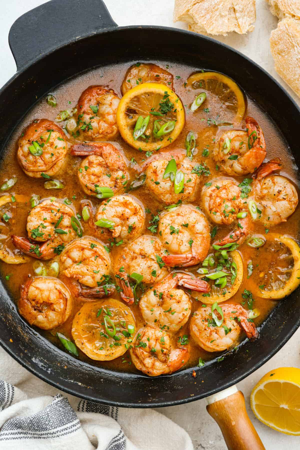 You have to make this New Orleans BBQ shrimp! The shrimp are tender and swimming in a rich, buttery garlic sauce. Grab a bib, lick your fingers, and sop up every last drop with crusty bread. Cooked and garnished New Orleans BBQ shrimp in a skillet.
