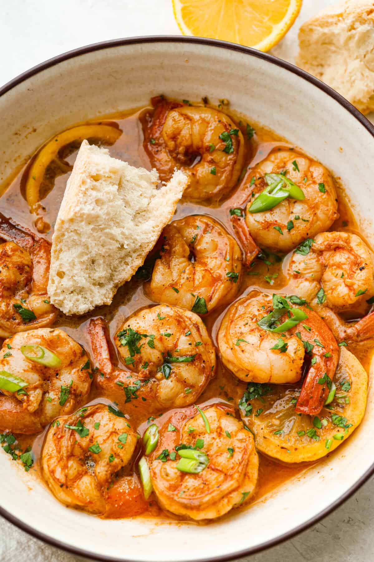 You have to make this New Orleans BBQ shrimp! The shrimp are tender and swimming in a rich, buttery garlic sauce. Grab a bib, lick your fingers, and sop up every last drop with crusty bread. Plated New Orleans BBQ shrimp with a wedge of crusty bread.