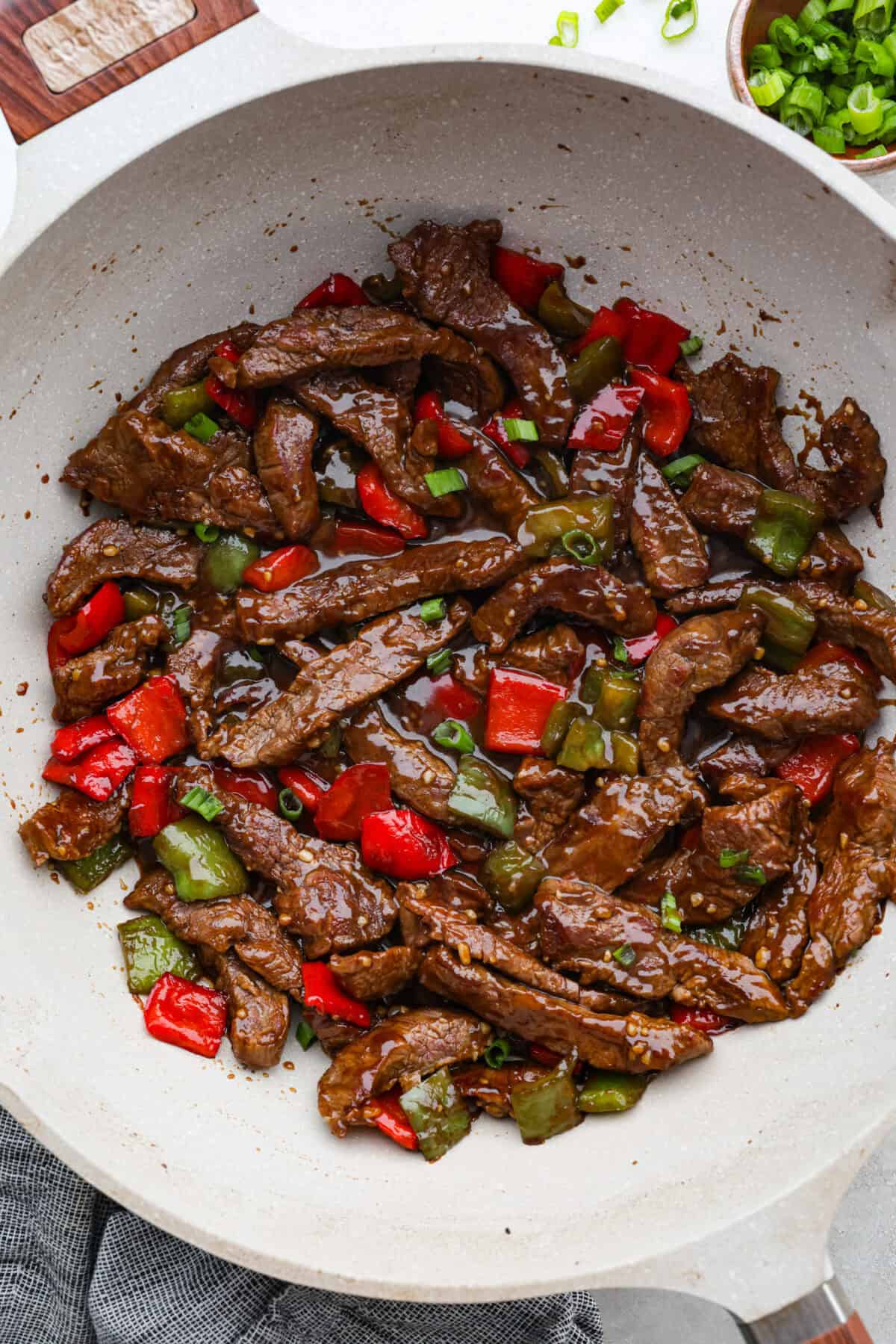Trust me on this one. If you want the most tender pepper steak you’ve ever made at home, this recipe is it. It’s fast, saucy, and I give you just enough tips to make it work on a busy night! Overhead shot of pepper steak completely cooked and in the wok garnished with green onions.