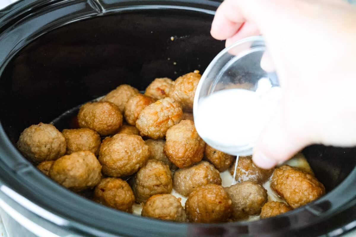 Slow cooker bourbon meatballs are an easy, set-it-and-forget-it favorite. Frozen meatballs simmer in a sweet, sticky bourbon sauce, making them perfect for an appetizer or a simple dinner with just 10 minutes of prep. Someone adding the cornstarch slurry to the crockpot.