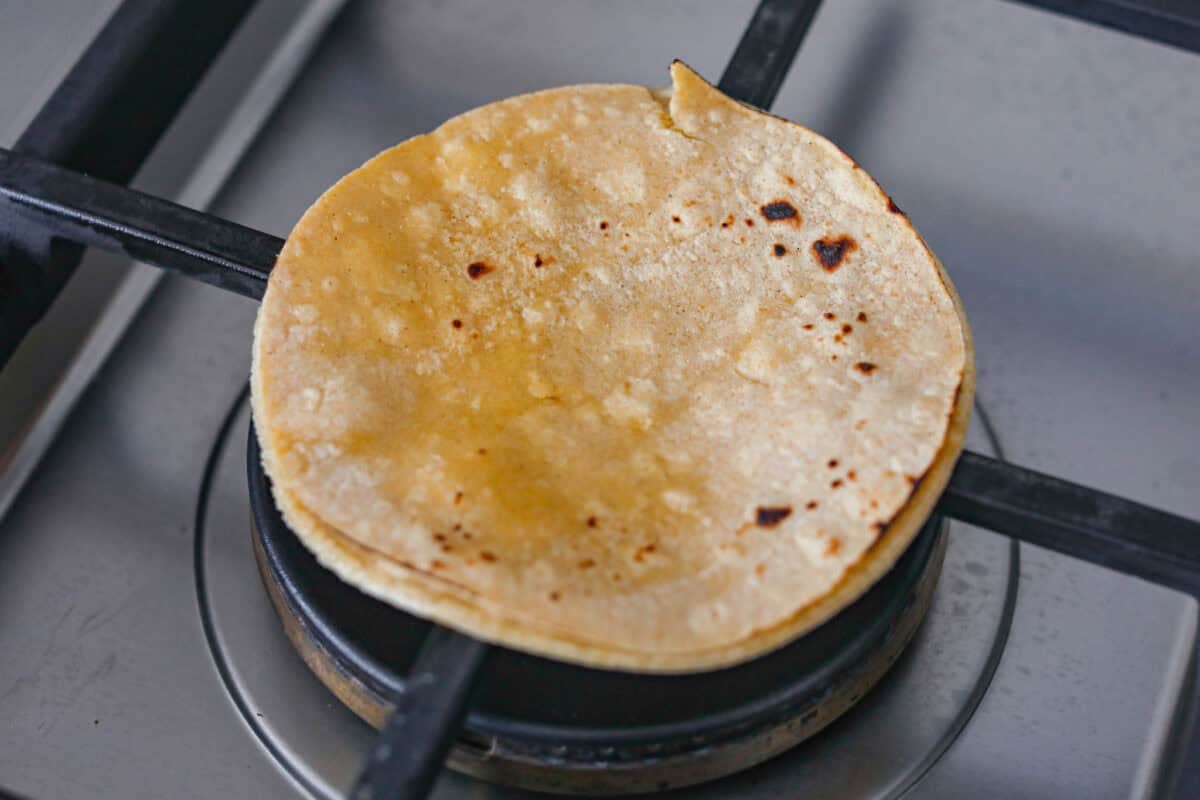 Get ready to be instantly obsessed with these crack chicken tacos! They are loaded with creamy ranch chicken, crispy bacon, and melty cheddar for a can’t-stop-eating dinner that disappears fast. Corn tortillas being cooked on a gas burner.