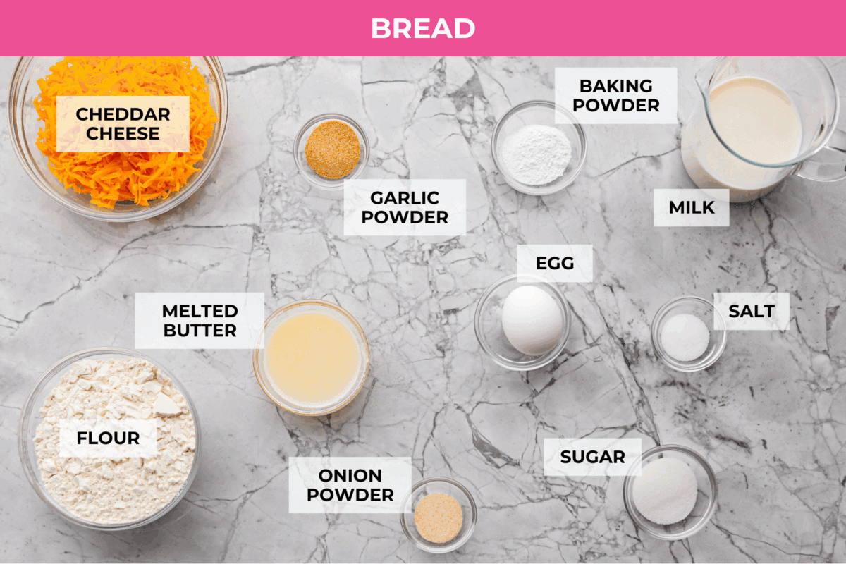 If you love my Red Lobster Biscuits, this Cheddar Bay Biscuit Bread has the same buttery, garlicky cheddar flavor, just mixed and baked right in a bread pan. Slice it warm and serve it with basically anything. It's a must-make! Trust me! Overhead shot of labeled bread ingredients.