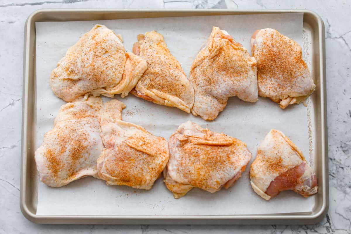 This Irish chicken is my cozy mashup of pub vibes and weeknight reality. Seared chicken thighs baked over bacon, cabbage, and potatoes, then I add a splash of Irish whiskey and a touch of cream to make the whole pan taste extra special. Seasoned chicken thighs on a piece of parchment paper lined baking sheet.