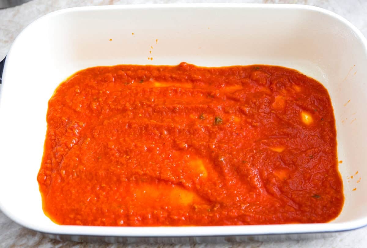 My classic manicotti is a reader favorite, so I wanted to make a version with a little more protein. Sausage is one of my favorite pasta add-ins, and it keeps this new Sausage Manicotti budget-friendly, hearty, cheesy, and so satisfying. Marinara sauce added to the bottom of a baking dish.