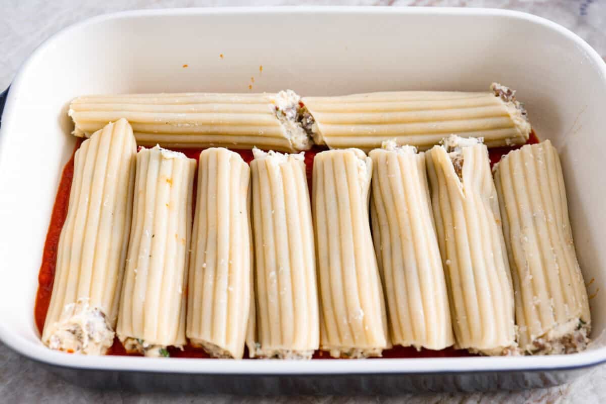 My classic manicotti is a reader favorite, so I wanted to make a version with a little more protein. Sausage is one of my favorite pasta add-ins, and it keeps this new Sausage Manicotti budget-friendly, hearty, cheesy, and so satisfying. Stuffed manicotti shells in a baking dish on top of the marinara sauce.