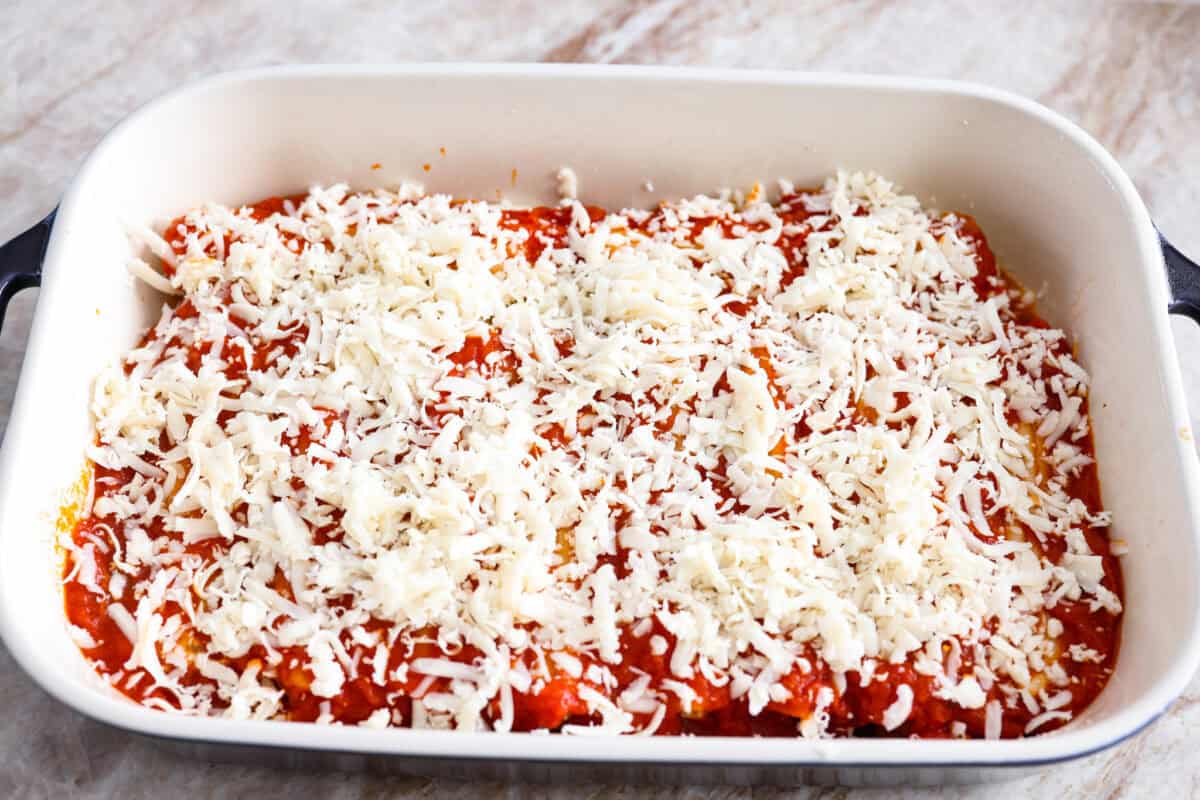 My classic manicotti is a reader favorite, so I wanted to make a version with a little more protein. Sausage is one of my favorite pasta add-ins, and it keeps this new Sausage Manicotti budget-friendly, hearty, cheesy, and so satisfying. Marinara sauce and shredded cheese on top of the stuffed manicotti.