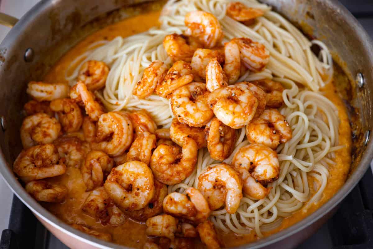 Bang bang shrimp pasta is what weeknight dinner dreams are made of! Juicy shrimp, tender pasta, and that irresistible sweet-and-spicy bang bang sauce come together in just 20 minutes. It’s creamy, bold, and guaranteed to be a hit. Shrimp and pasta added to the bang bang sauce in the skillet.