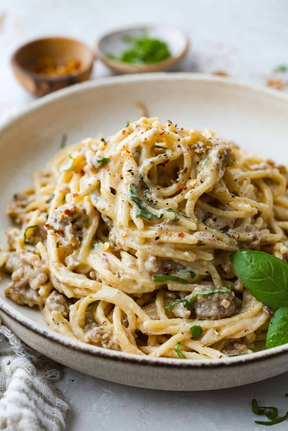 Plate of creamy sausage spaghetti garnished with basil leaves. 