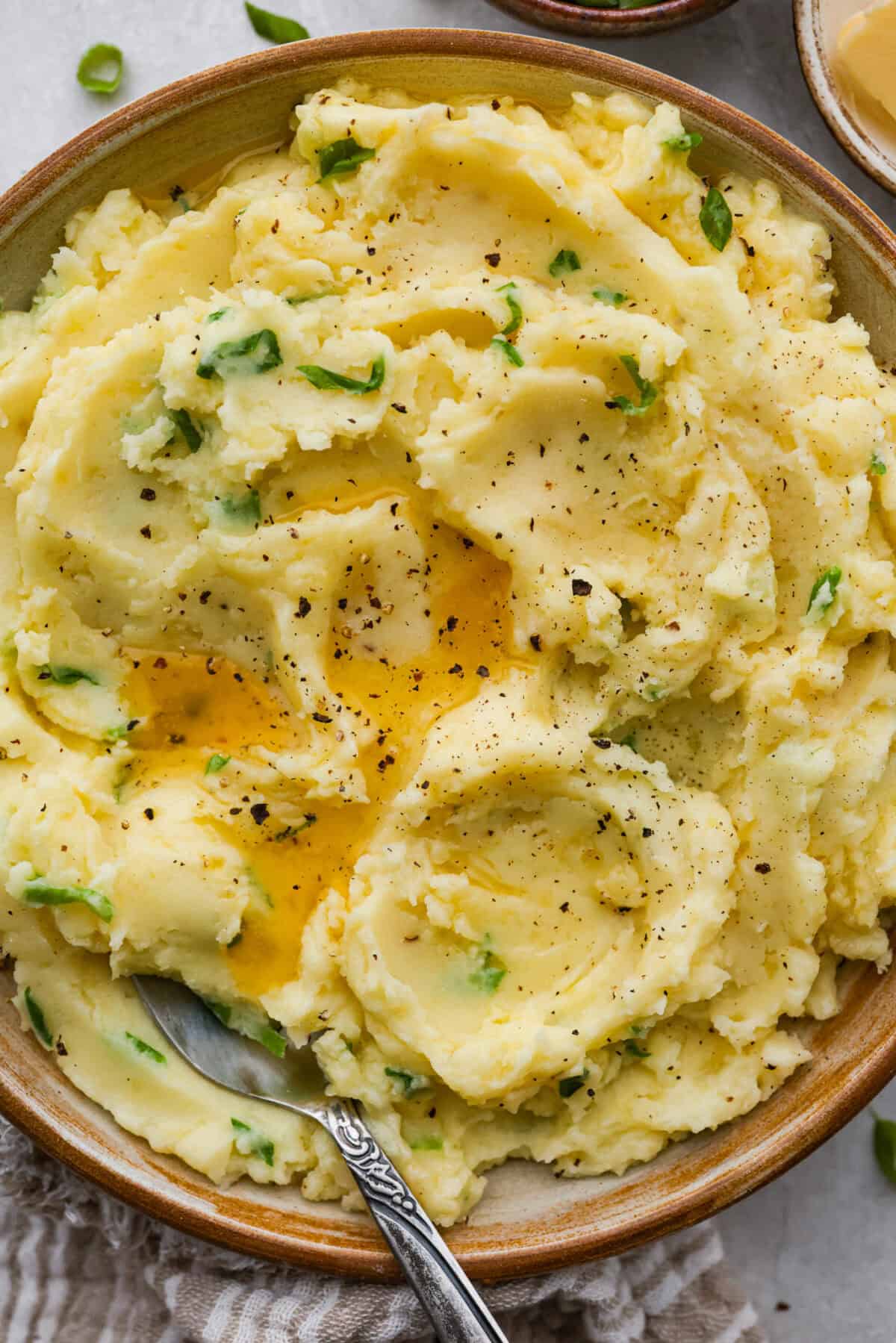 Irish champ potatoes are mashed potatoes done right. Fluffy spuds meet warm onion kissed milk and a generous melt of Irish butter for a side that’s simple, rustic, and seriously so good! Bowl of Irish champ potatoes, with melted butter and slat and pepper.