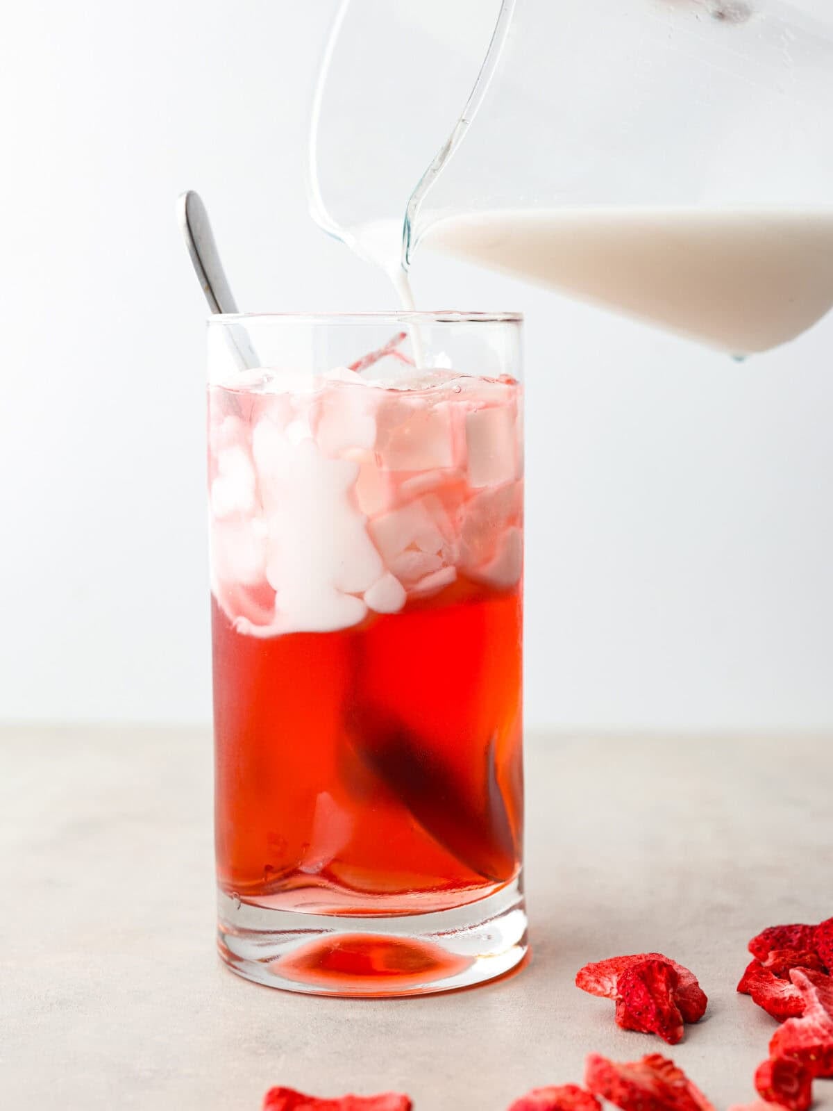 You guys, Starbucks sells the Strawberry Aรงaรญ concentrate in stores! Which means we can make the famous Starbuck's Pink Drink at home! And let me tell you, it's spot on! With just three ingredients, it's ridiculously easy to make year-round, and so good! Someone pouring coconut cream into a glass with strawberry acai concentrate.