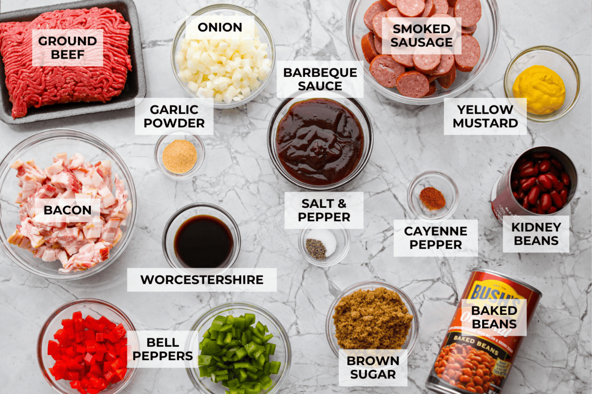 If you're bringing a dish to the cookout, make it these loaded baked beans. Three kinds of meat, two kinds of beans, and a sauce that is smoky, sweet, and full of depth. They disappear every single time. Overhead shot of labeled loaded baked beans ingredients.
