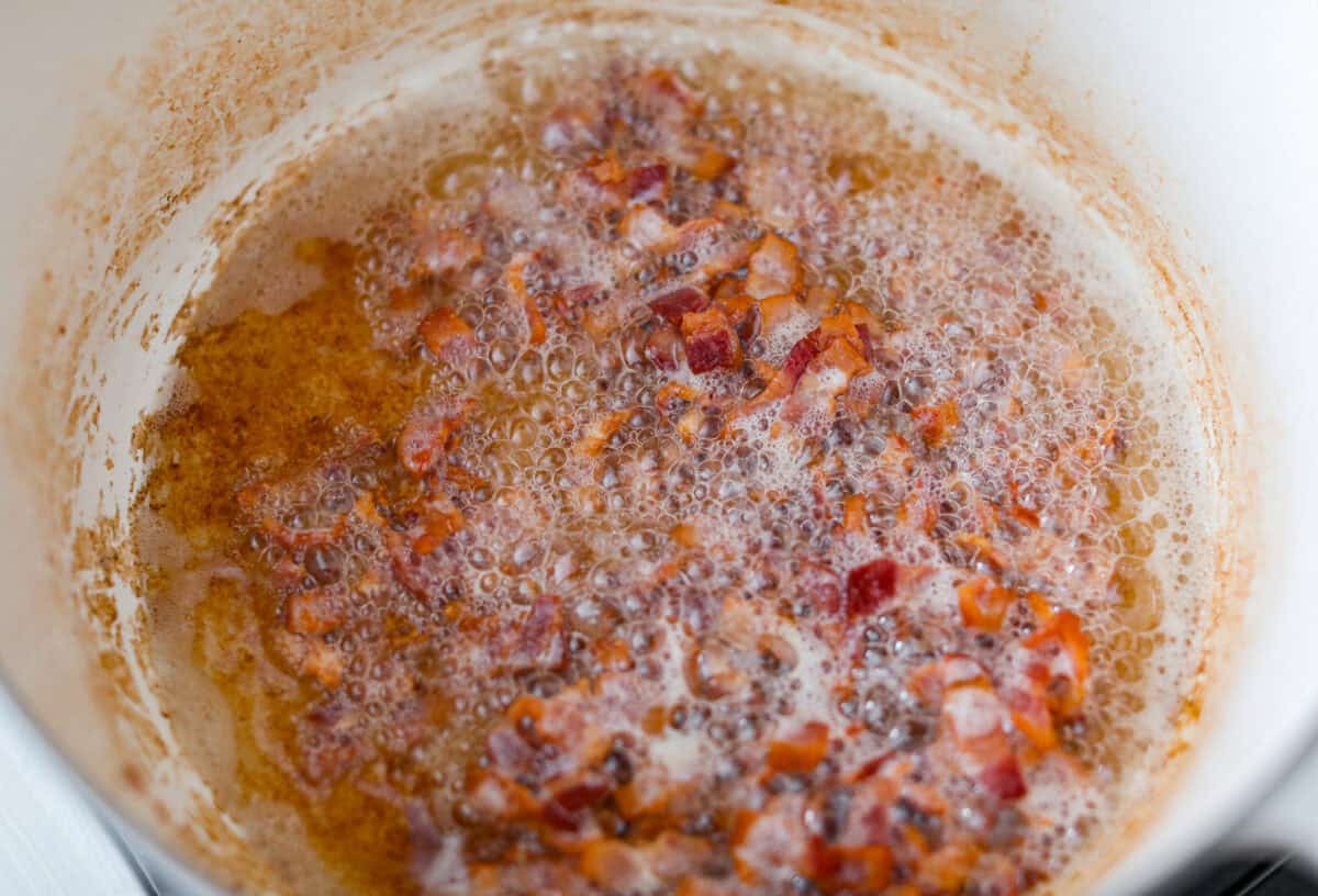 If you're bringing a dish to the cookout, make it these loaded baked beans. Three kinds of meat, two kinds of beans, and a sauce that is smoky, sweet, and full of depth. They disappear every single time. Bacon cooking in a large pot.