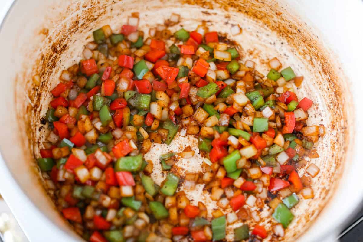 If you're bringing a dish to the cookout, make it these loaded baked beans. Three kinds of meat, two kinds of beans, and a sauce that is smoky, sweet, and full of depth. They disappear every single time. Veggies cooking in bacon grease in a large pot.