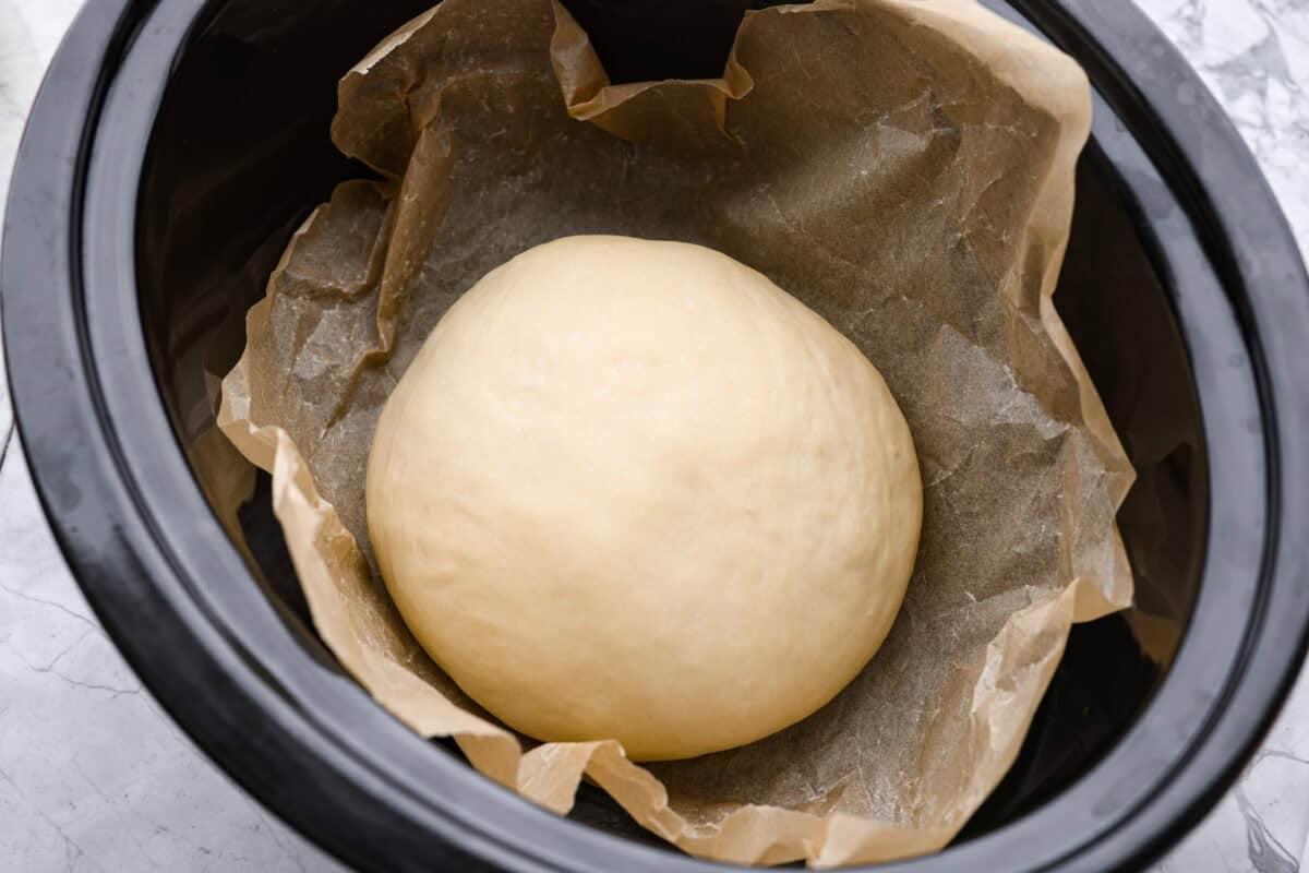 If you’ve ever wanted homemade bread without all the work, this slow cooker bread is my favorite easy trick. As a busy mom, I love that a few simple ingredients and my slow cooker turn into a warm, soft loaf with hardly any effort. Ball of dough added to the crockpot on top of a piece of parchment paper.