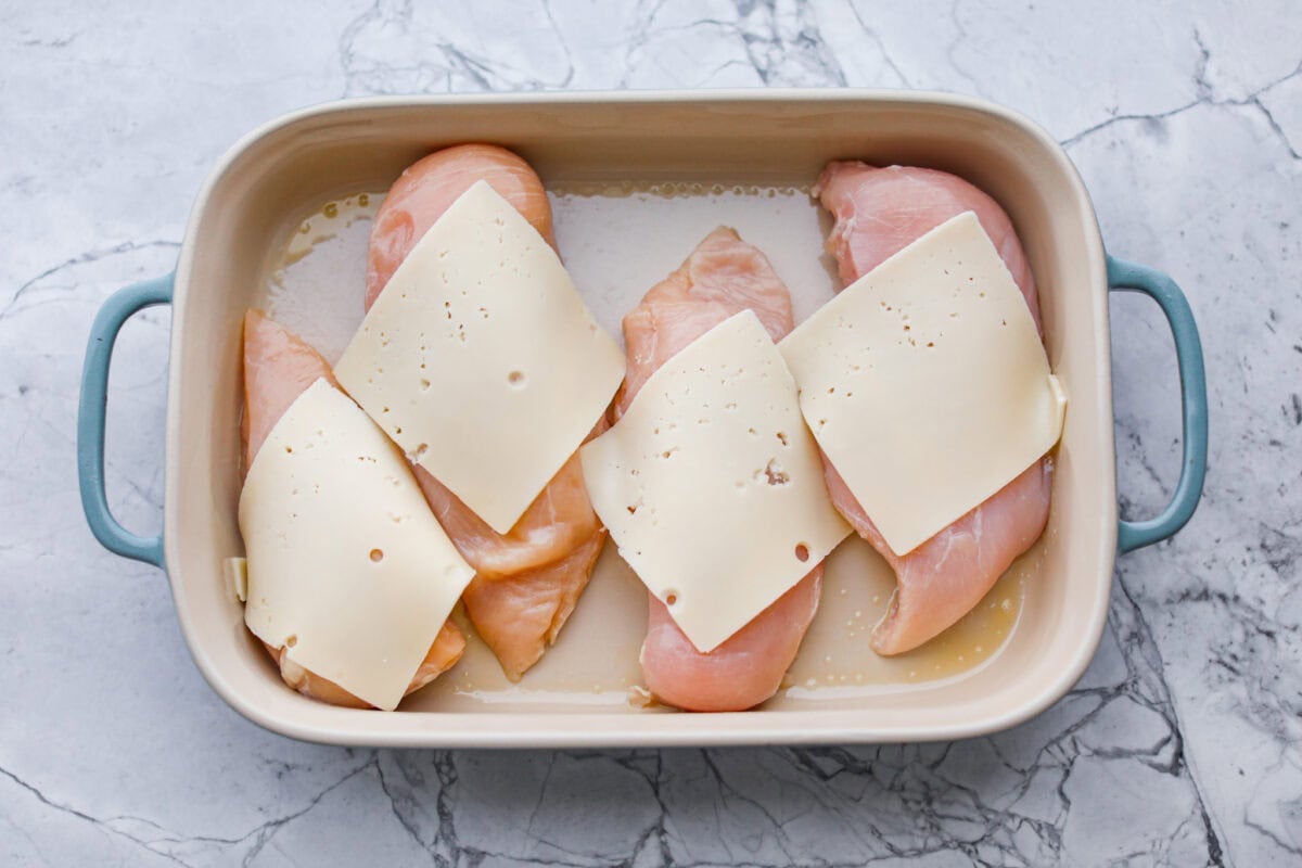 Okay, this Swiss Chicken Casserole is my go-to when I donโt feel like cooking. You basically throw it together, pop it in the oven, and somehow end up with super tender chicken, melty Swiss cheese, and the creamiest sauce. Chicken breasts in the bottom of a baking dish with a slice of Swiss cheese on top.