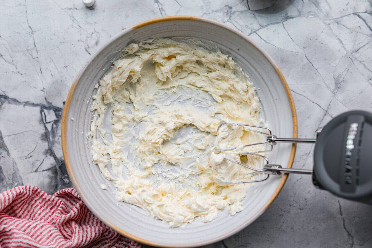 Fluff salads never go out of style. They're light, creamy, and just plain fun! This cherry cheesecake fluff is customizable and so easy to throw together! It's packed with sweet-tangy cheesecake flavor and juicy cherries in every bite. Cream cheese mixed in a bowl with a hand mixer.