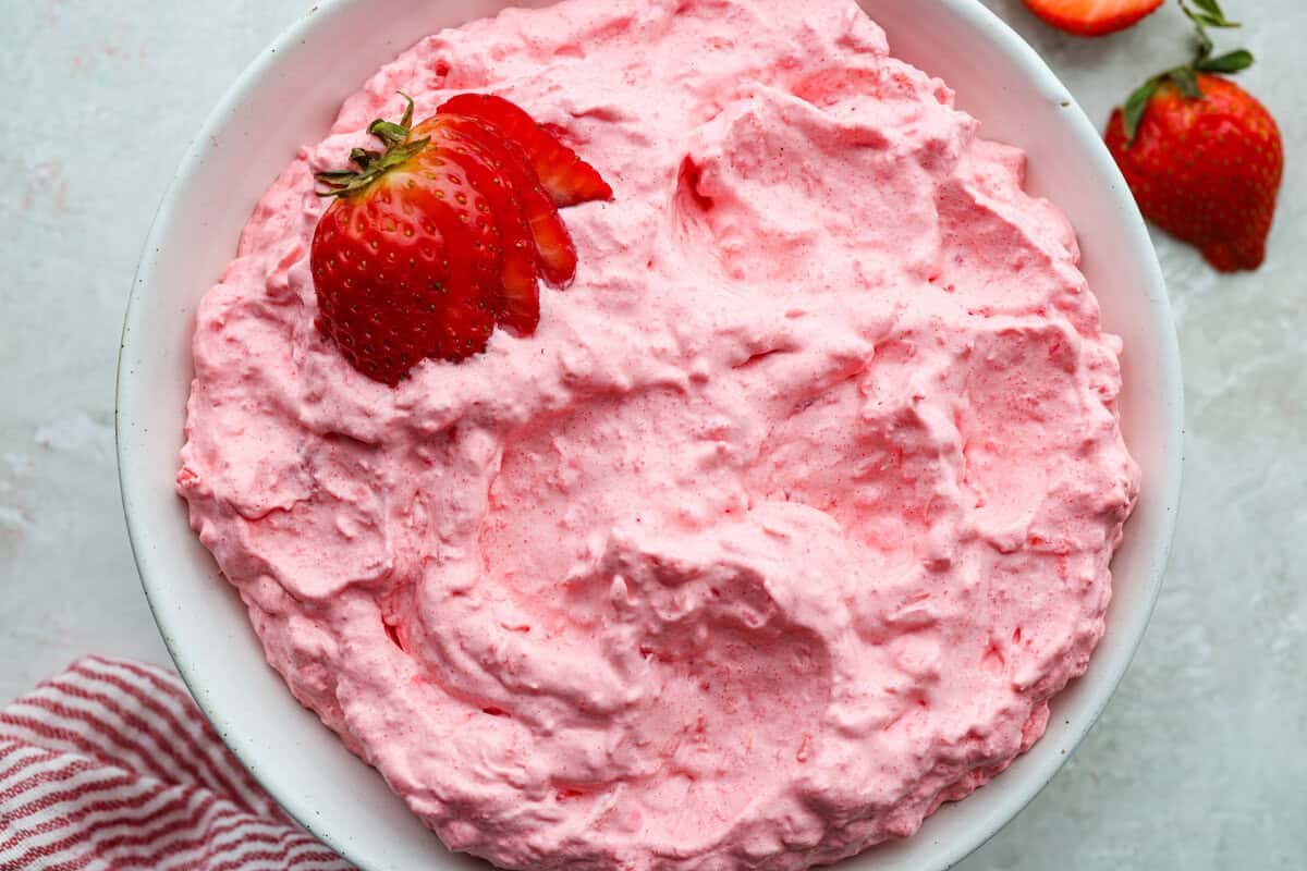 This cottage cheese jello salad is one of those old-school recipes that never really goes out of style. My dad absolutely loves it and requests it all the time, especially for family get-togethers. Itโs creamy, fruity, and ridiculously easy to make. Serving bowl full of cottage cheese jello salad garnished with sliced strawberries.