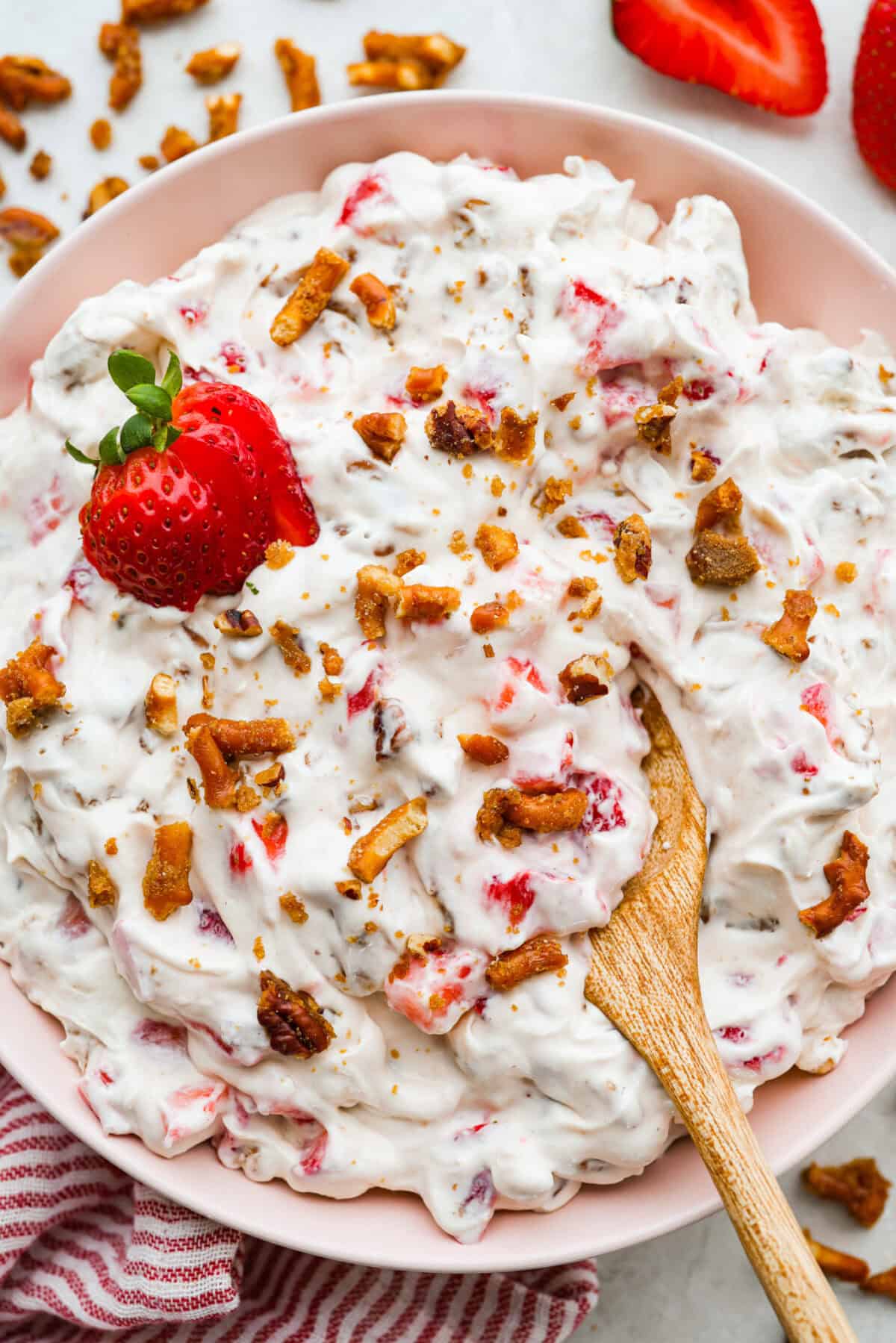 Crack pretzel salad is the shortcut version of my popular strawberry pretzel salad! It has all the sweet, salty, creamy goodness you love, but this version comes together in less than 15 minutes for an easy dessert everyone goes crazy for. Large bowl of crack pretzel salad with wooden spoon and garnished with a strawberry.