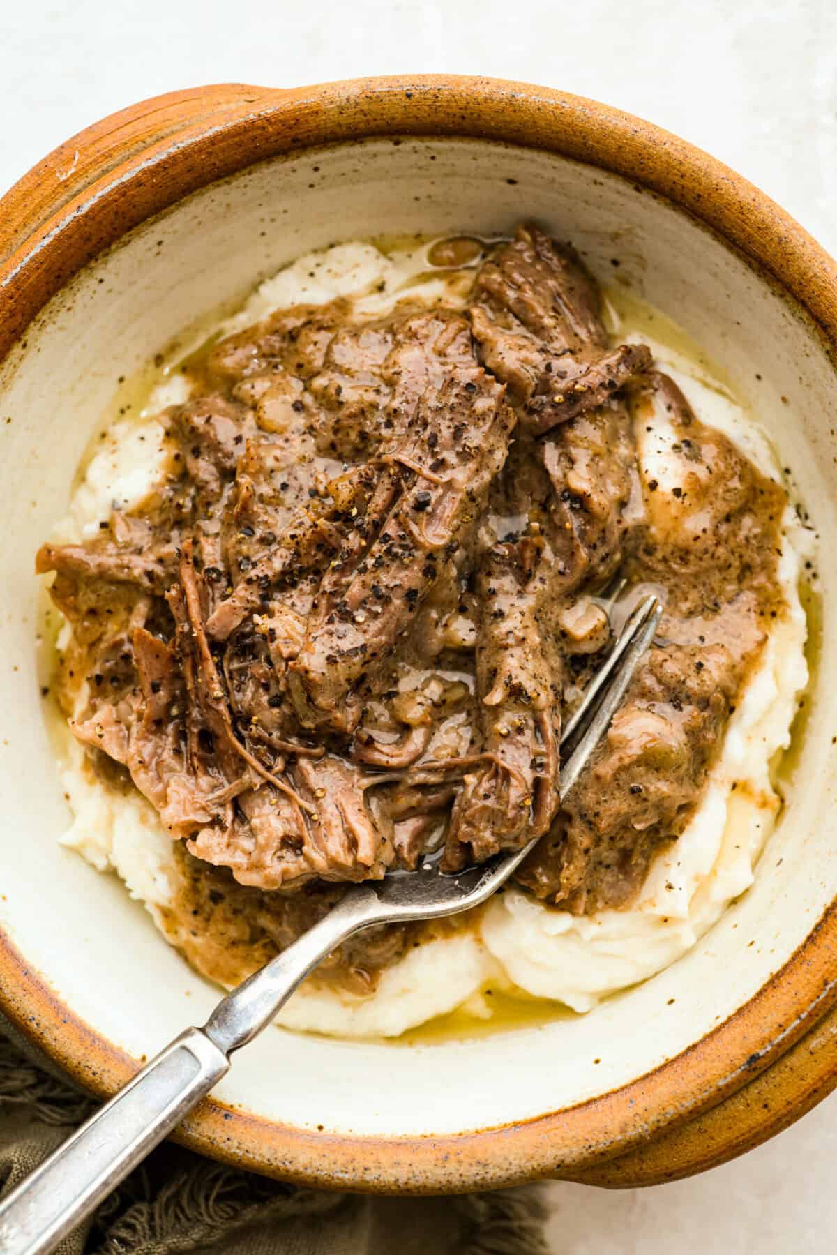This 4 Ingredient Mushroom Beef is just like how my grandma used to make her Sunday roast, simple and cozy. You toss it all in the crockpot, and it comes out melt in your mouth tender with a rich gravy thatโs perfect over everything. Serving of 4 ingredient mushroom beef in a bowl over mashed potatoes.