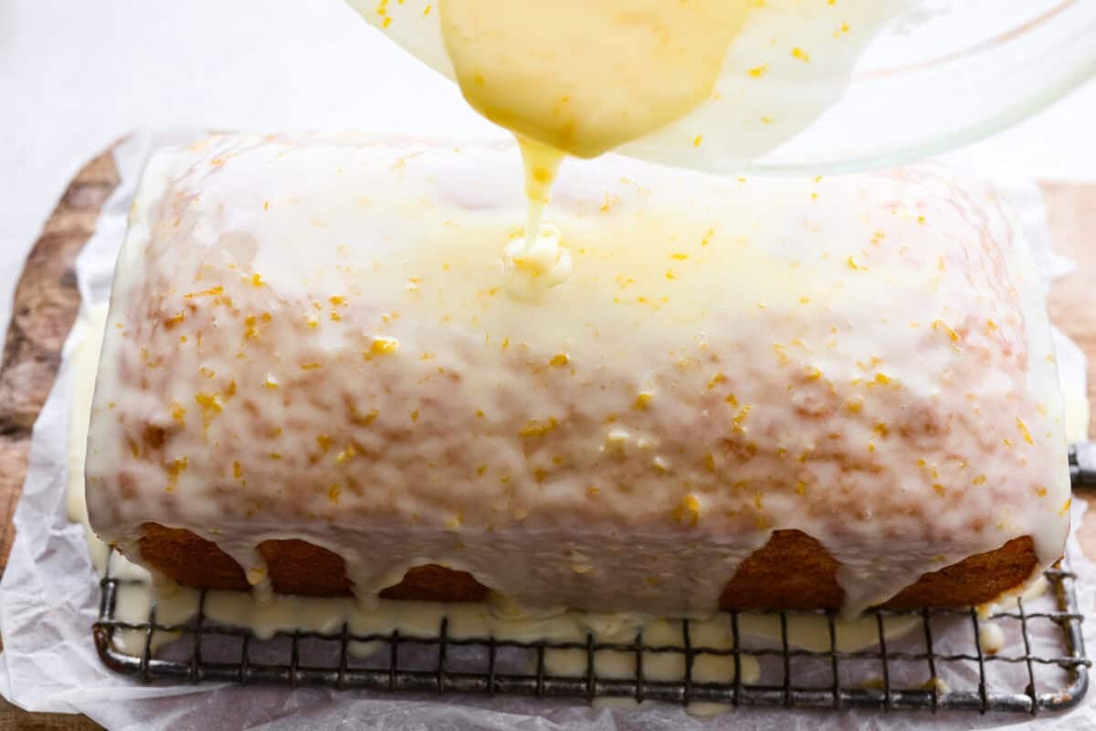 This glazed orange loaf is sunshine in every slice! Fresh orange zest and juice give it a bright citrus flavor. It's just like this incredibly popular Lemon Loaf. It’s the kind of quick bread you keep coming back to for just one more slice. Someone pouring the orange glaze over the baked orange loaf.