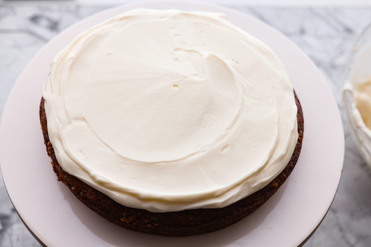If you’ve never had hummingbird cake, just know it’s one of those cakes people take a bite of and immediately ask for the recipe. It’s soft, sweet, packed with banana and pineapple, and topped with a cream cheese frosting that is to die for! First layer of hummingbird cake with a layer of frosting on top.