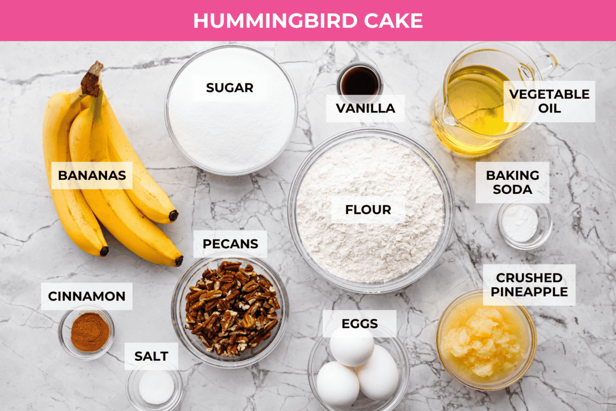 If you’ve never had hummingbird cake, just know it’s one of those cakes people take a bite of and immediately ask for the recipe. It’s soft, sweet, packed with banana and pineapple, and topped with a cream cheese frosting that is to die for! Overhead shot of labeled hummingbird cake ingredients.