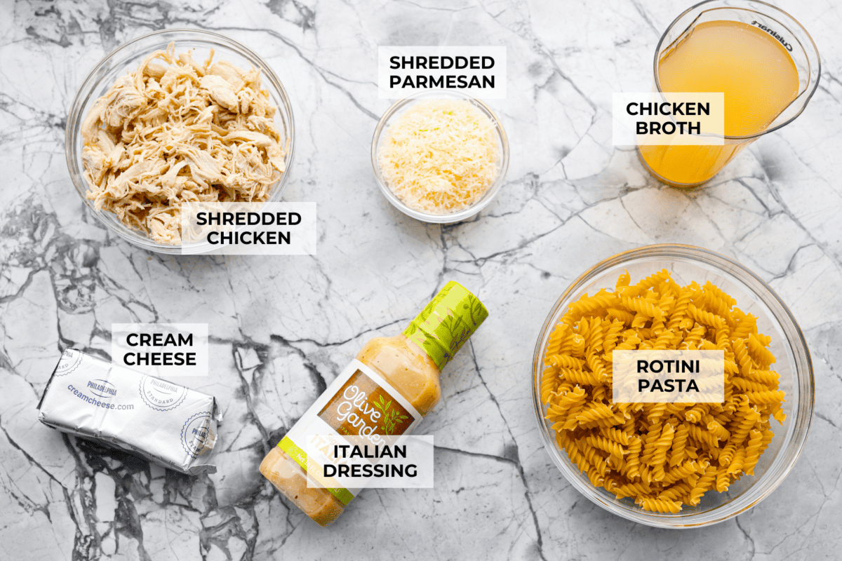 This baked Olive Garden chicken is pure comfort food made easy! It uses Olive Garden Italian dressing and just 5 other ingredients to create a creamy, cheesy pasta bake everyone loves. Quick prep, one dish, and big flavor in every bite! Overhead shot of labeled ingredients.
