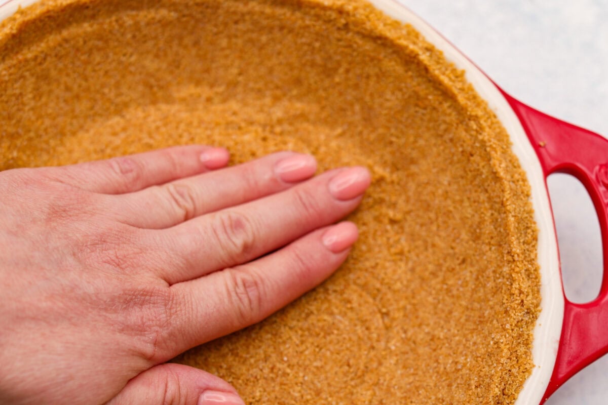 When itโs too hot to even think about turning on the oven, this no bake strawberry cream pie is exactly what you want waiting in the fridge. Itโs cool, creamy, loaded with fresh strawberries, and comes together without heating up your kitchen Someone smashing the crust ingredients into the bottom of the pie dish.
