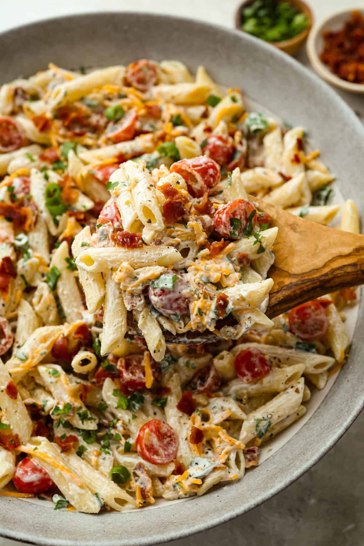 If there’s one side dish that disappears fast, it’s this million dollar pasta salad. It’s packed with crispy bacon, sharp cheddar, fresh veggies, and a creamy dressing that ties it all together. It’s sure to steal the spotlight at any table! Someone taking a large spoonful of million dollar pasta salad out of the large serving bowl.