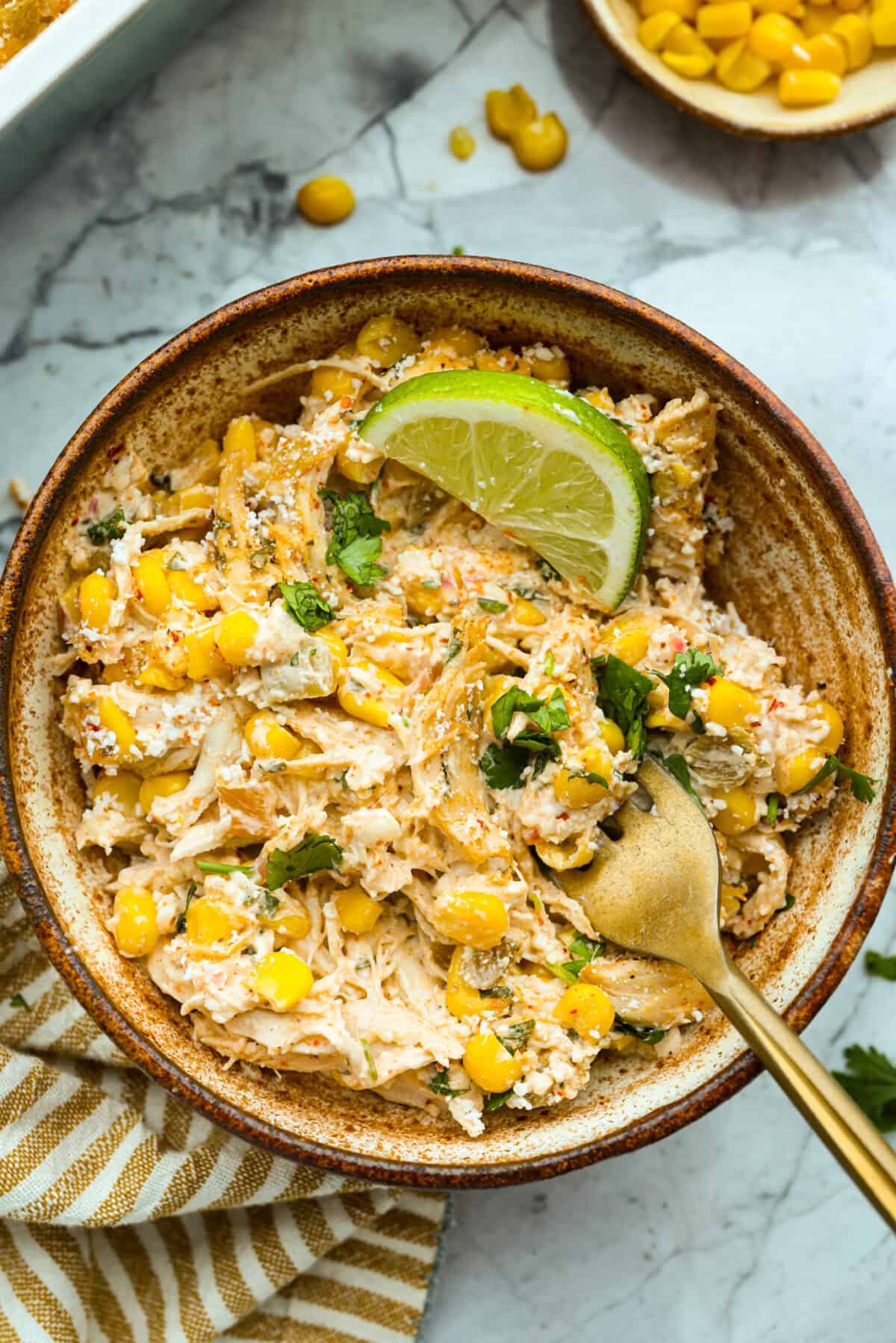 This Mexican Street Corn Chicken Casserole takes everything you love about elote, tangy lime, smoky Tajin, and creamy cotija, and turns it into one bubbly, cheesy weeknight dinner the whole family will devour! Serving of the Mexican street corn chicken casserole in a bowl with a gold fork.