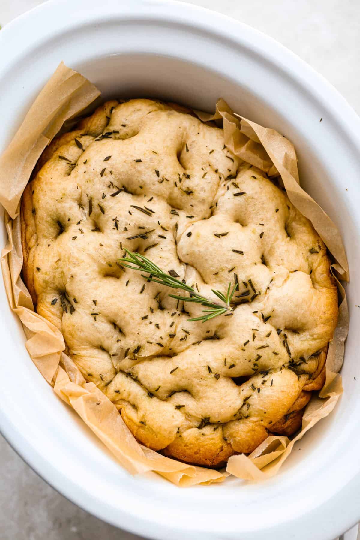 This slow cooker focaccia is the easiest way to get homemade bread on the table! Frozen dinner rolls transform into a pillowy, herb-flecked loaf with barely any effort. Just drizzle, dimple, and let your slow cooker do the rest. Image of the slow cooker focaccia bread in the crockpot.