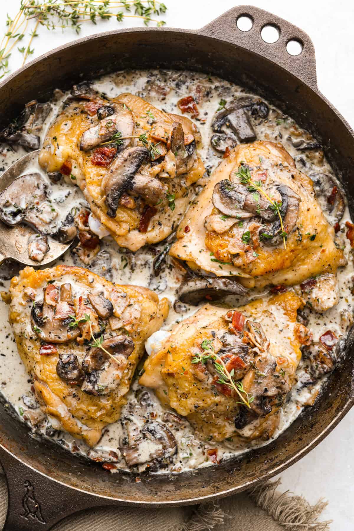 Skillet with bacon mushroom thyme chicken thighs cooked and covered in a creamy mushroom sauce. 