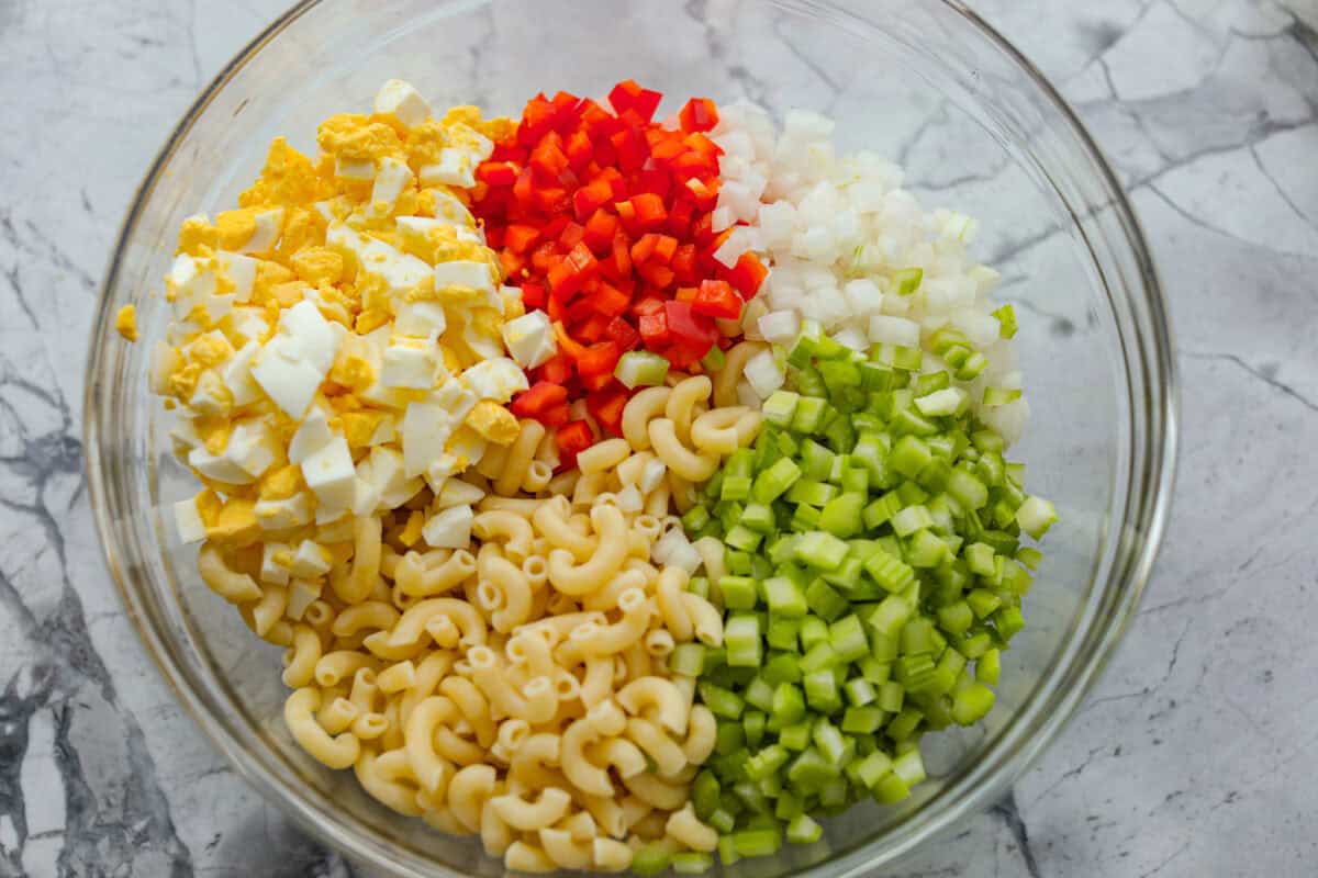 There’s something delightfully old school about Amish pasta salad. The sweet, tangy dressing, the macaroni, the chopped eggs, the crunchy celery. It tastes like the kind of recipe that’s been living in a handwritten church cookbook for decades. Bowl full of pasta salad ingredients.