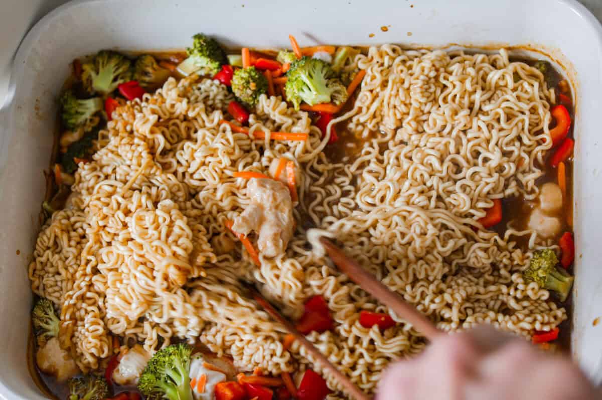 I kept seeing this dump and bake ramen all over my feed and finally had to try it for myself! Turning family favorite ramen into a cozy baked dinner was an immediate hit! It's so good with tender noodles, colorful veggies, and a savory sauce! Stirring the partially baked dump and bake ramen together with chopsticks.