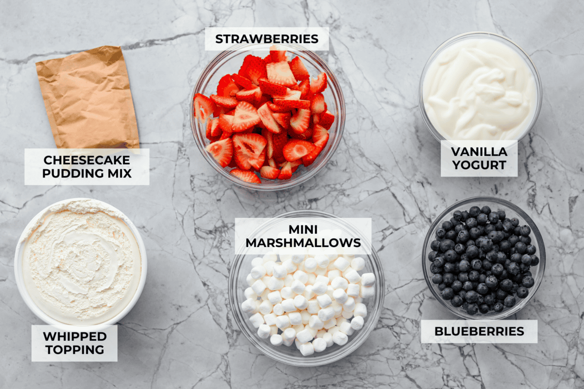 This red, white, and blue cheesecake salad is the fun summer side dish everyone goes back for. Itโs creamy, fluffy, packed with berries and marshmallows, and so easy to bring to a BBQ, potluck, or Fourth of July party. Overhead shot of labeled red white and blue cheesecake salad ingredients.