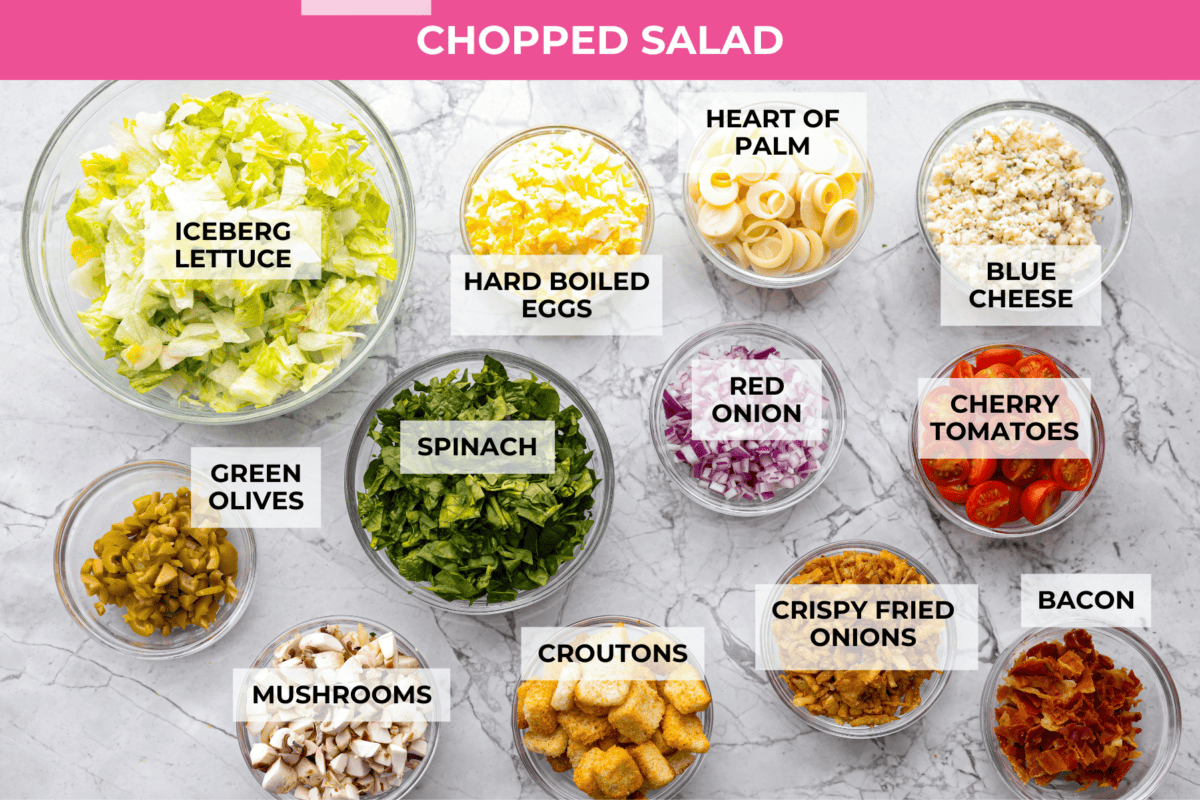 Ruth's Chris chopped salad is a steakhouse legend, and now you can make it at home for a fraction of the price. Crisp greens, smoky bacon, bold blue cheese, and a tangy lemon basil dressing come together in one showstopping bowl that tastes just like the real thing. Overhead shot of labeled Ruth's Chris chopped salad ingredients.