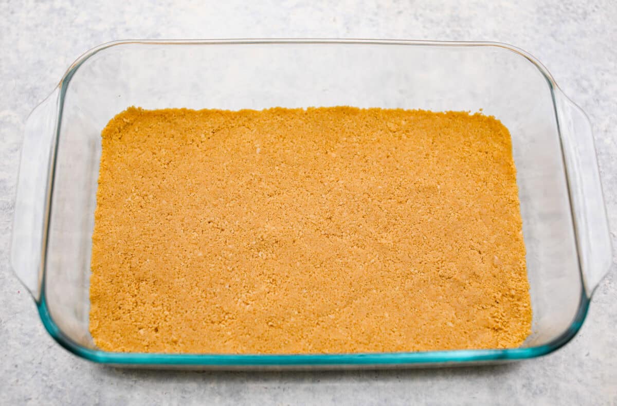 Orange creamsicle lush is sunshine in dessert form! With creamy orange layers, a buttery golden Oreo crust, and bright fresh citrus flavor, this easy no-bake dessert is a fun twist on my popular Lemon Lush thatโs perfect for summer. Cookie crust in the bottom of a 9x13 pan for the orange creamsicle lush dessert.