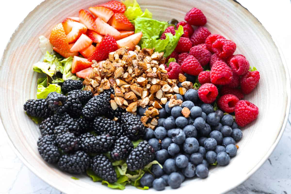 This copycat Zupa’s Nuts About Berries Salad is fresh, bright, and full of texture in every bite. Loaded with sweet berries, crunchy cinnamon almonds, crisp greens, and creamy poppyseed dressing, it tastes just like the restaurant favorite right at home! Large bowl with salad ingredients added to it.
