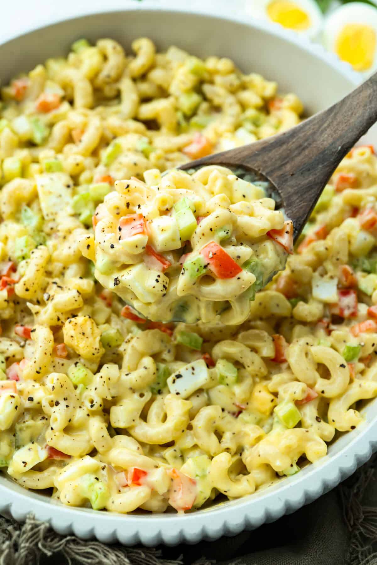 There’s something delightfully old school about Amish pasta salad. The sweet, tangy dressing, the macaroni, the chopped eggs, the crunchy celery. It tastes like the kind of recipe that’s been living in a handwritten church cookbook for decades. Someone lifting a scoop of Amish pasta salad out of the bowl.