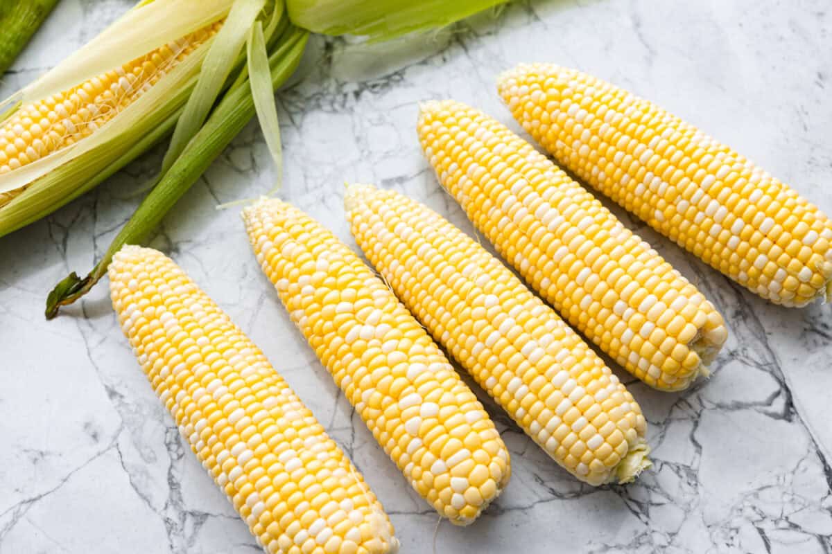 Grilled corn is simple and so versatile. Eat it straight off the cob with butter, cut it intoย salads,ย casseroles, or serve it chilled. The sweet kernels with a touch of smoky char are pure summer heaven. Ears of corn all lined up with their husks removed.
