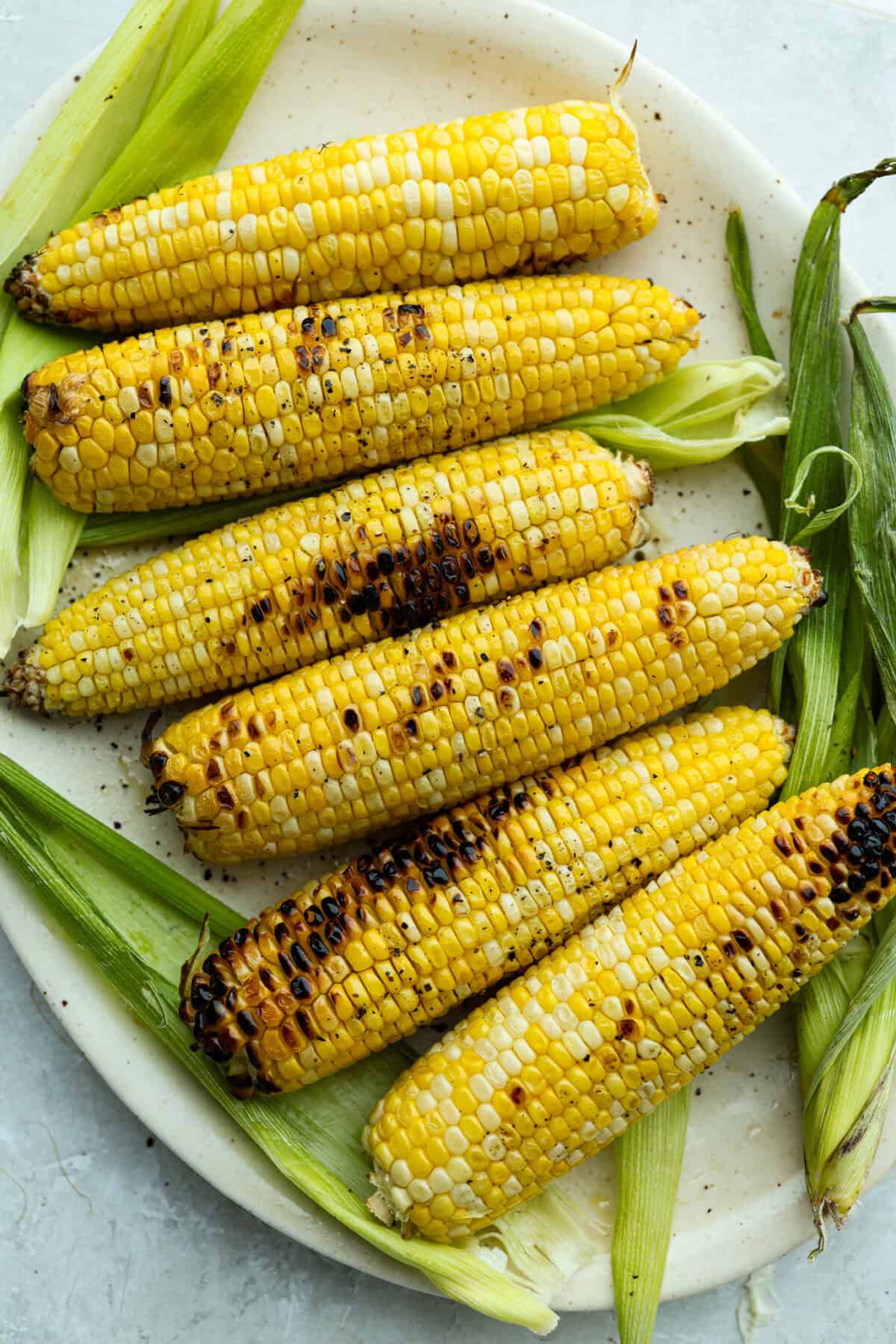 Grilled corn is simple and so versatile. Eat it straight off the cob with butter, cut it intoย salads,ย casseroles, or serve it chilled. The sweet kernels with a touch of smoky char are pure summer heaven. Plate of grilled corn cobs.