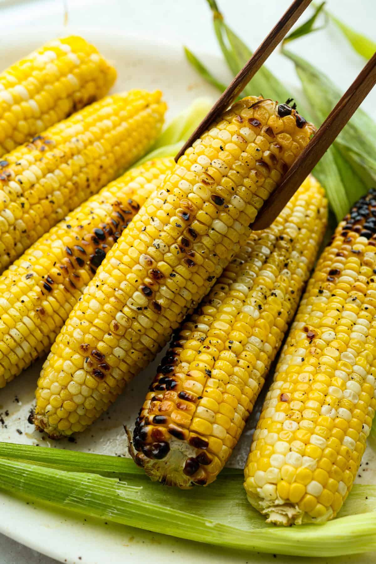 Grilled corn is simple and so versatile. Eat it straight off the cob with butter, cut it intoย salads,ย casseroles, or serve it chilled. The sweet kernels with a touch of smoky char are pure summer heaven. Someone lifting a grilled corn cob off a plate of grilled corn.