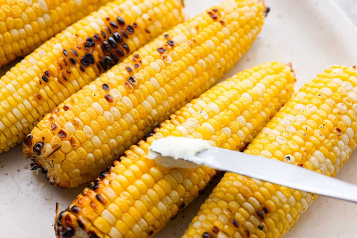 Grilled corn is simple and so versatile. Eat it straight off the cob with butter, cut it intoย salads,ย casseroles, or serve it chilled. The sweet kernels with a touch of smoky char are pure summer heaven. Someone spreading butter on the grilled corn.